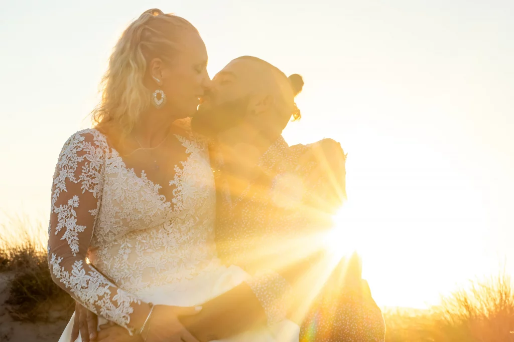photographie de mariage prise en couché de soleil, les deux mariés s'embrassent tandis que l'on peut voir le soleil illuminé les deux parties sur le côté de l'image