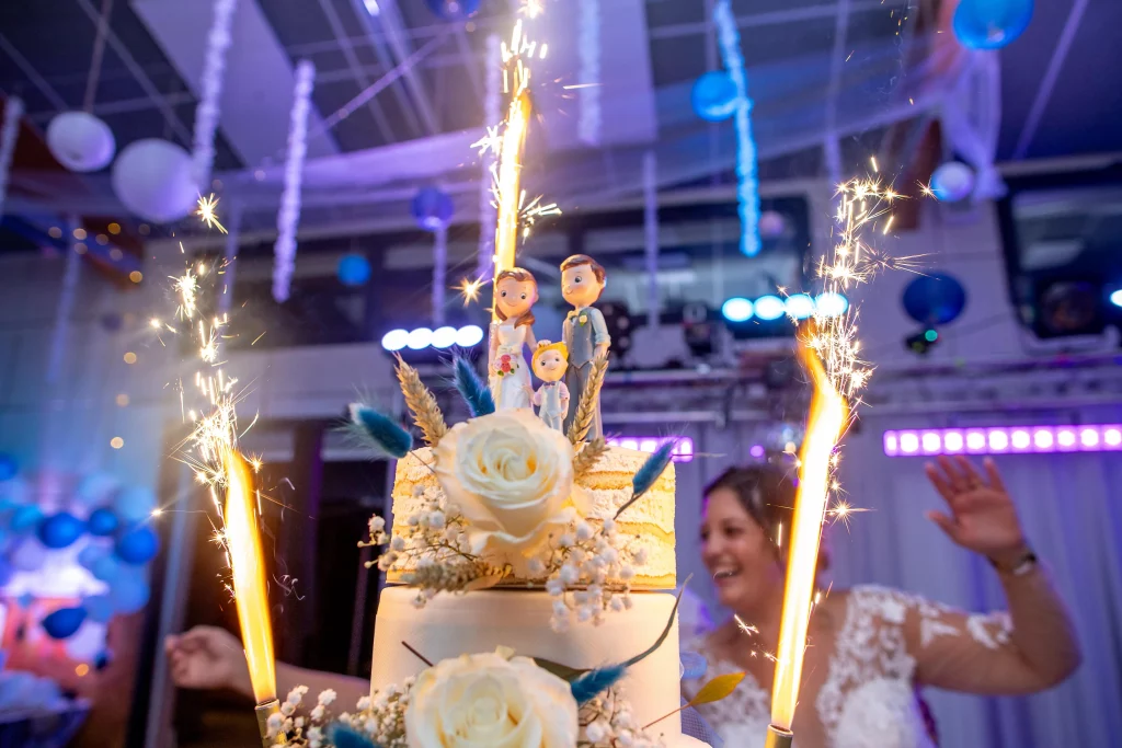 Photographe de mariage, photo du gâteau lors d'un mariage, avec les bougies fontaines en fond et les statuettes des deux mariées en premier plan