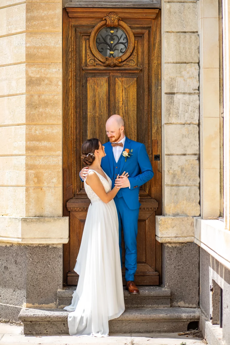 couple de marié durant la séance de couple qui se regarde mutuellement avec en arrière plan une magnifique porte de château en face à face, photographier par un photographe de mariage.