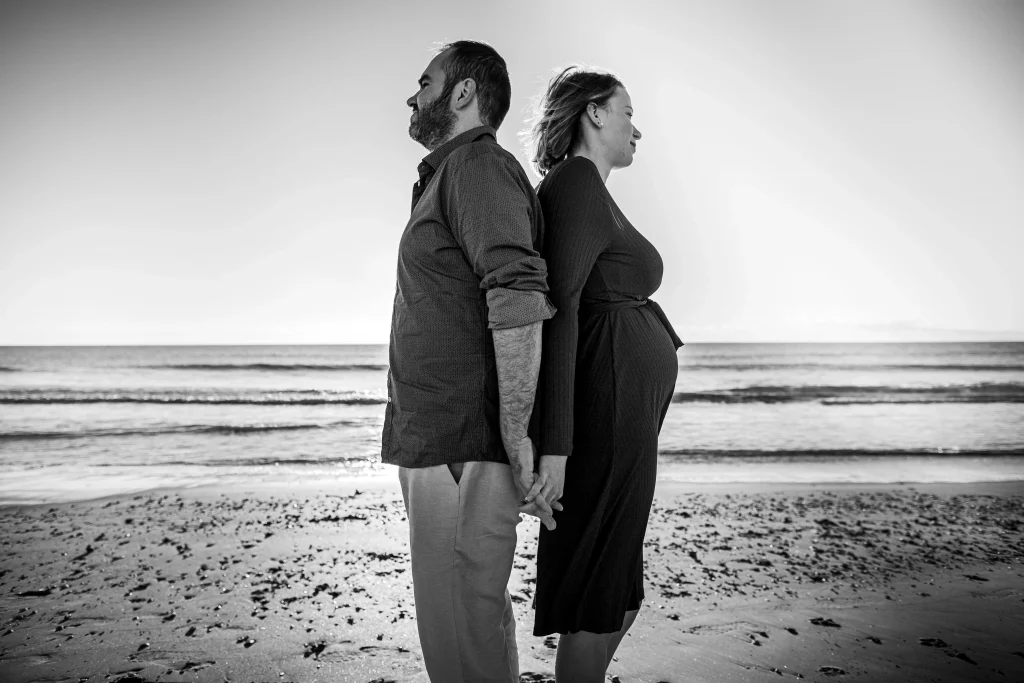 photo de grossesse, le couple est dos à dos sur la plage