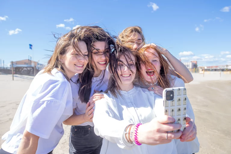 Photographe spécialisé evjf sur la plage de Palavas dans l'Hérault. Les filles tiennent leurs téléphones en faisant un selfie avec les cheveux dans le vent