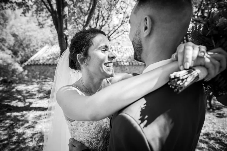 Mariée qui rigole durant la séance de couple avec les bras croisés autour du coup du marié. Photographie en noir et blanc faite par un photographe pro