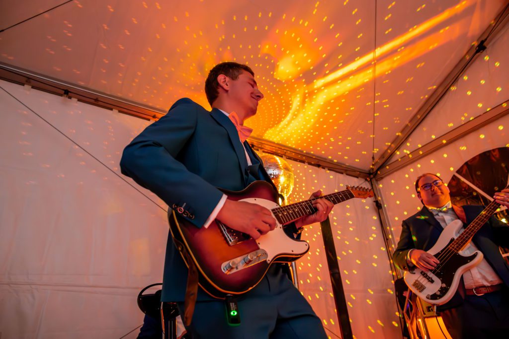 Photo de mariage de Agnès et Thibault. Thibault joue de la guitare en costume bleu, avec une superbe lumière orange derrière et son témoin à droite. Photographie de mariage faites par un photographe professionnel de mariage à Montpellier dans l'Hérault.