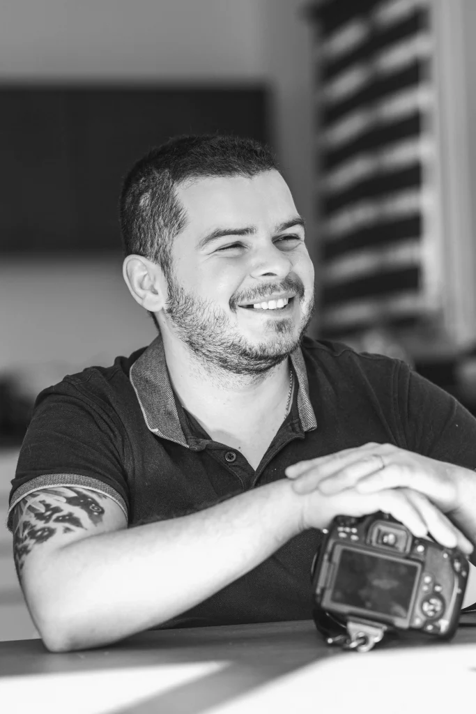 Portrait en noir et blanc de Romain Graille souriant avec son appareil photo.