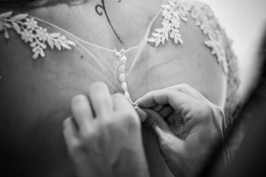photo de la dentelle de la robe de mariée avec la main de la témoin qui l'aide à fermer les boutons
