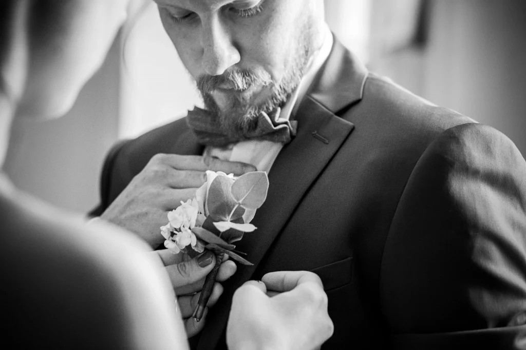 Photo de préparatif d'un mariage, la témoin mets la fleur au costume du marié