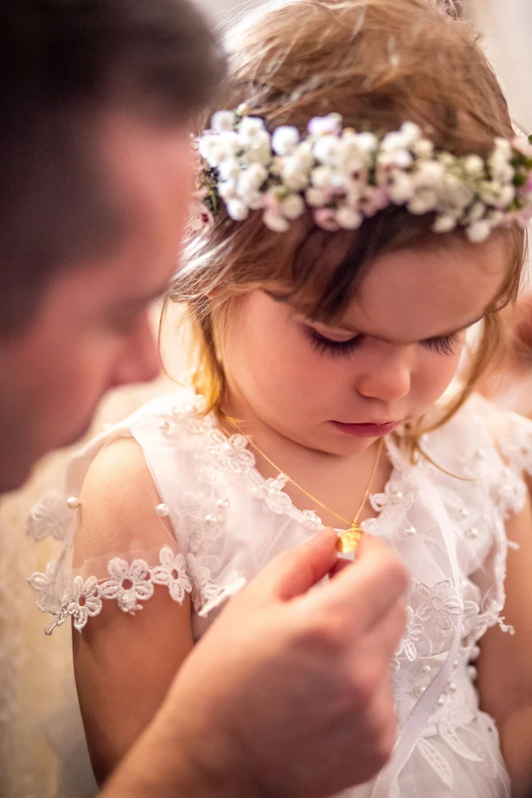 photographie professionnelle de baptême, la petite fille regarde le magnifique médaillon qu'elle a reçu et qui est accroché a son coup