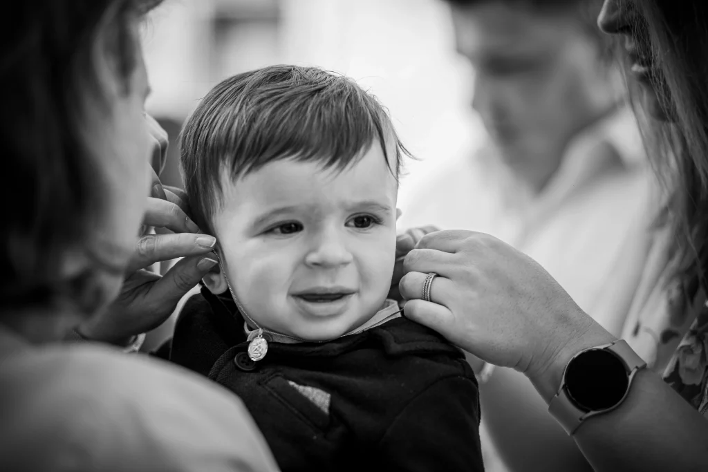 photo de baptême en noir et blanc la maman accroche le collier au coup de l'enfant