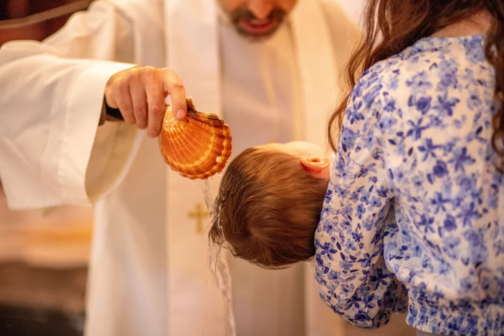 photographie professionnel de baptême, le prêtre verse l'eau bénite sur la tête de l'enfant