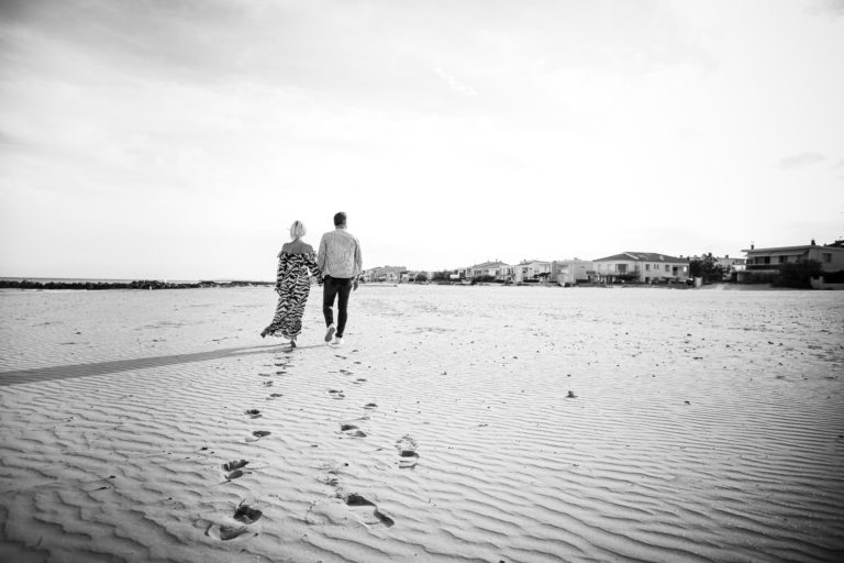 couple qui marche sur la plage, photo en noir et blanc de dos avec les pas qui mènent vers eux