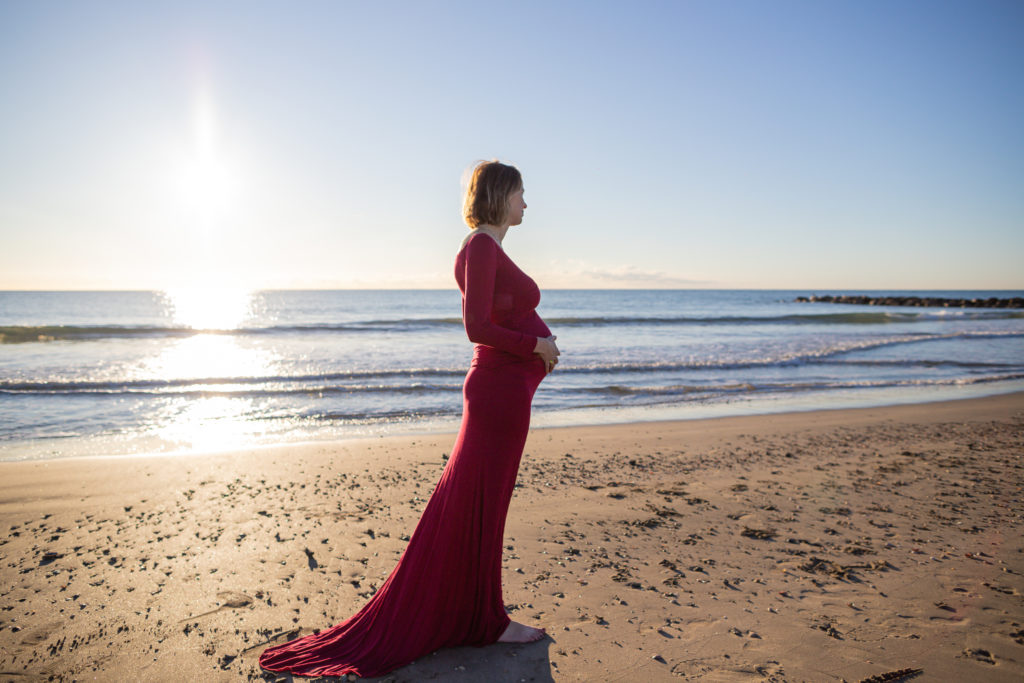 photo de grossesse sur la plage d'une femme dans une robe rouge