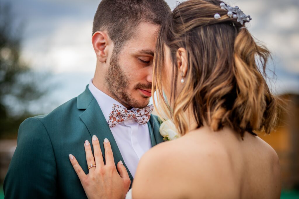 Photographie de Mariage de Ambre et Léo. Jeux du bouquet, ou la mariée lève le bouquet en l'air et doit couper une à une les ficelles de couleur ( rose, violet, vert ), la gagnante remporte le bouquet ! Photo prise en contreplongée, la mariée rit aux éclats dans sa belle robe blanche. Photographie prise par un photographe de mariage professionnel