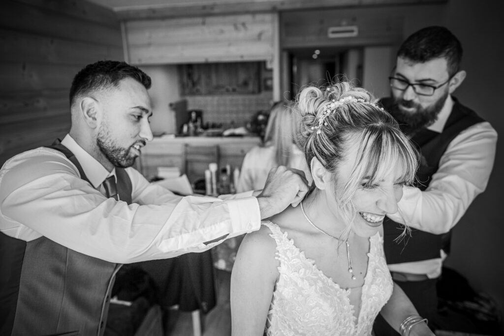 Photographie du mariage de Priscila et Steven dans l'hérault, la mariée se fait attaché sont collier par ses deux témoins, photo en noir et blanc