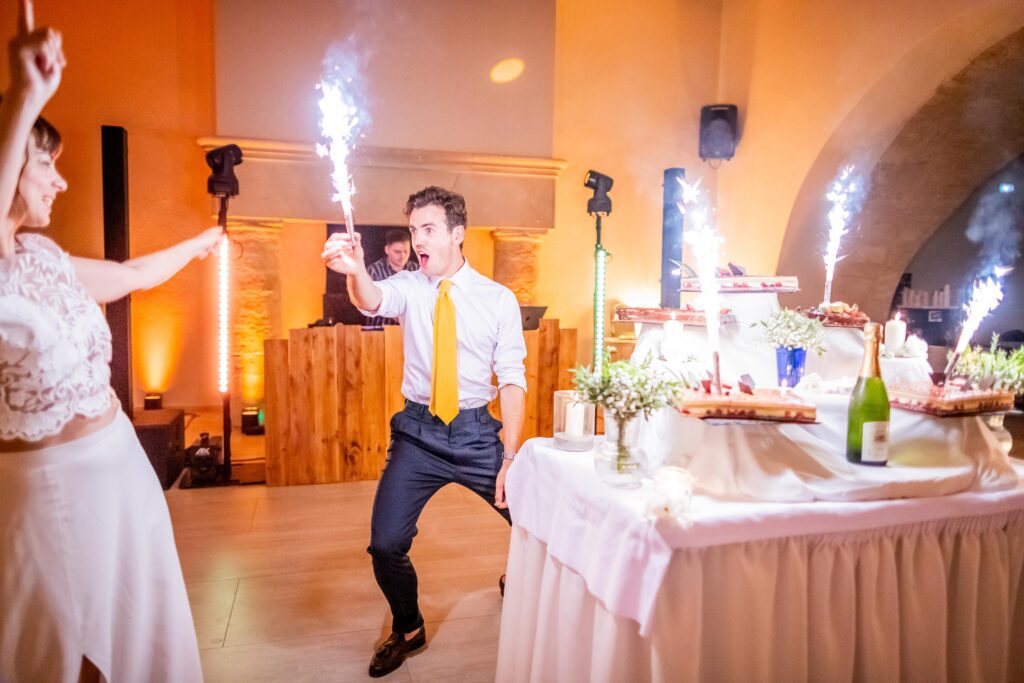 photographie de mariage de Mélanie et Alban, les mariées se promène dans la rue mains dans la mains, photographie en couleur , le marié à ouvert la bouteille de champagne qui coule dans le verre de la mariée qui est en dessosus, dans le gard