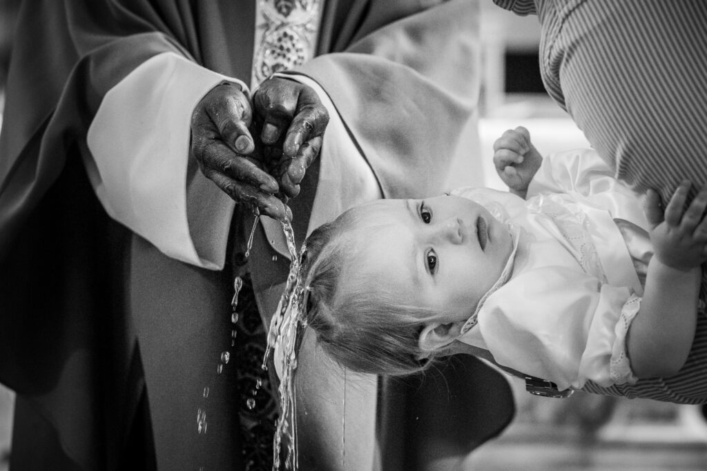 photographie de baptême religieux, le prêtre verse de l'eau sur la tête de l'enfant durant la cérémonie pour faire sa communion avec dieu