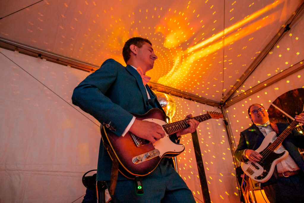 mariage de Astrid et pierre , photo du mariée durant la soirée qui joue de la guitare avec en fond une lumière orange, durant leurs mariage à Alès