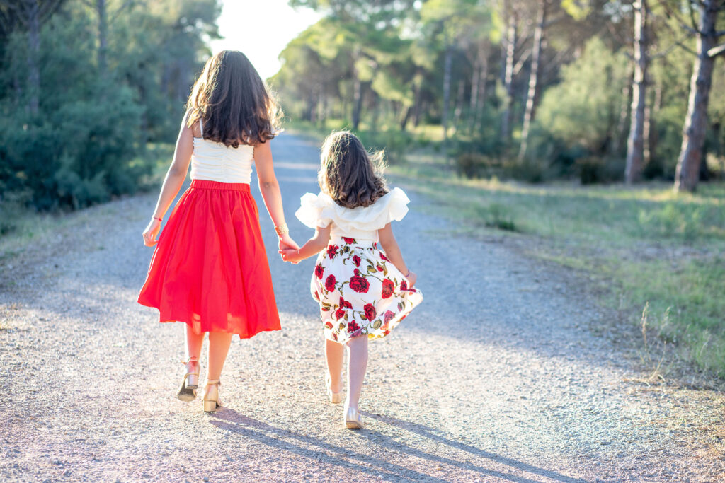 photographe famille à Montpellier. Deux petites filles en robe rouge, marche dans une allée boisé, photo de dos