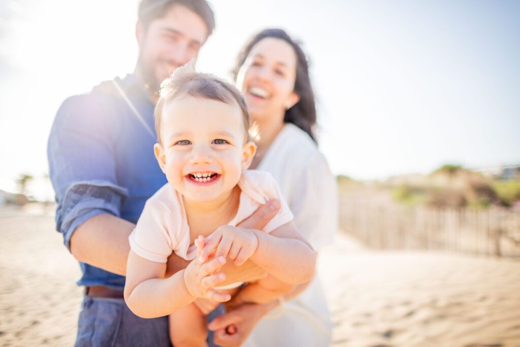 séance photo et shooting famille prise sur la plage par un photographe de famille photographe professionnel famille à Montpellier. Les parents mettent le bébé au premier plan et il rigole au éclat