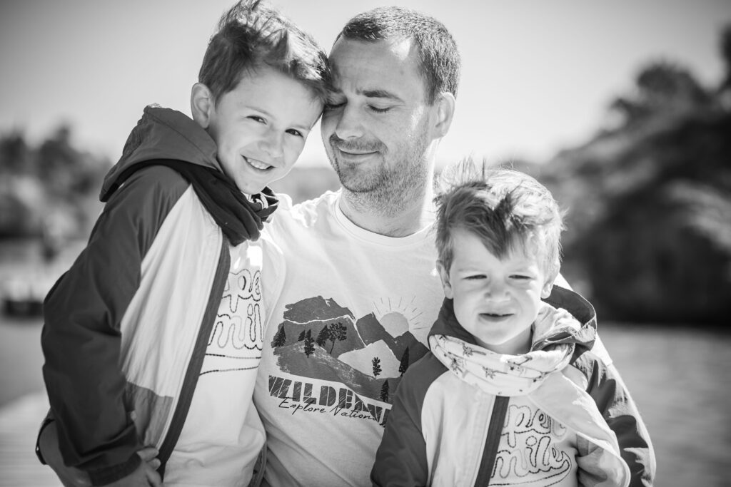 photographe famille à Nîmes, romain vous propose des images pleine de douceur et de sincérité, comme cette photo en noir et blanc d'un papa et ses deux garçon qui se font un câlin dans une magnifique photo en noir et blanc