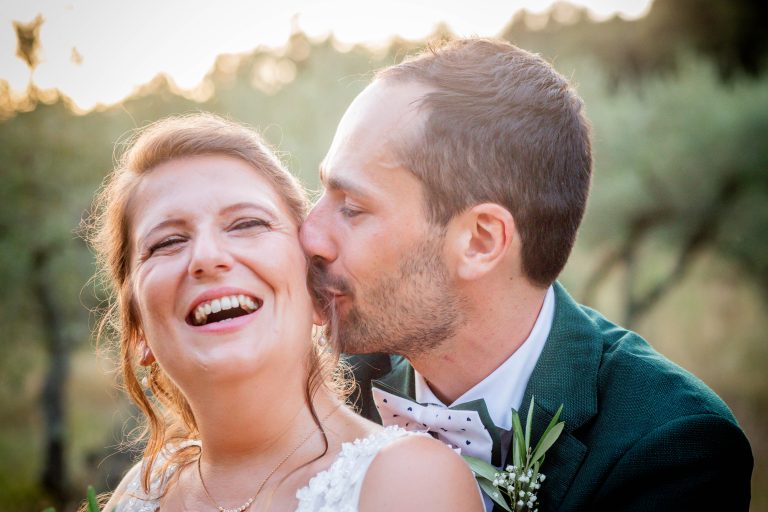 Victor embrasse Léa dans le cou pendant qu'elle éclate de rire lors de leur séance photo de couple au coucher du soleil.